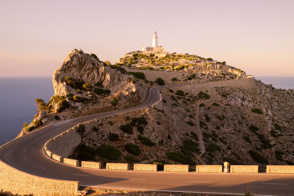 A road leading to a lighthouse with the sea and blue sky in the background