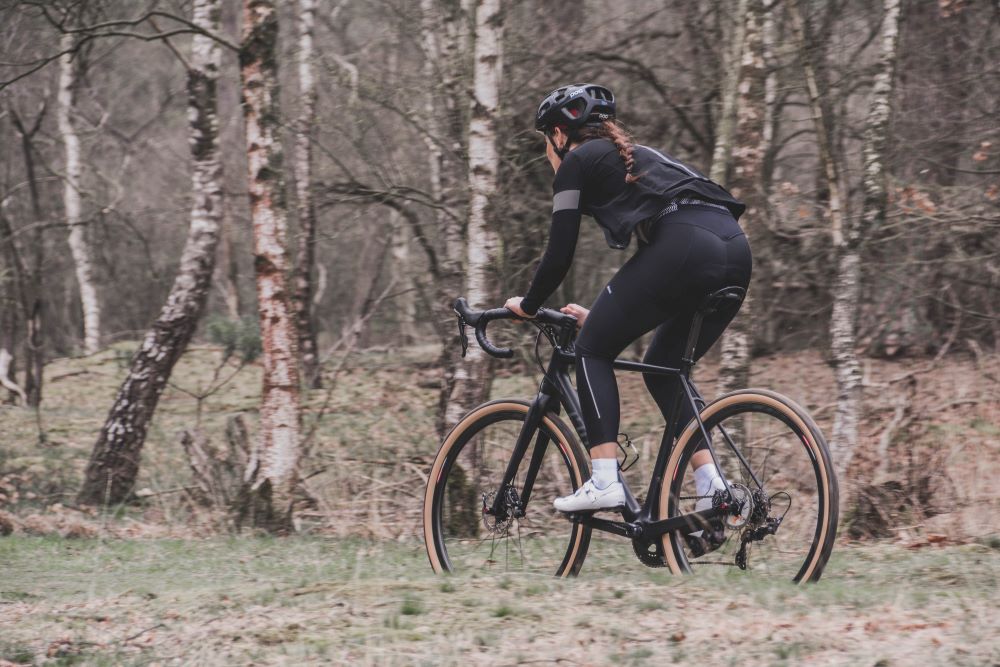 A woman riding a gravel bike near some trees